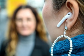 Nahaufnahme eines Ohres mit kabellosem Kopfhörer und Ohrring, gegenüber, unscharf, eine weitere Person