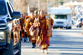 Eine Gruppe buddhistischer Mönche wandert , von Autos umgeben, über eine Straße