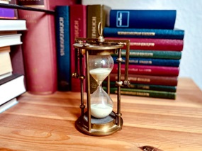 Regalbrett mit Stundenbüchern, davor eine Sanduhr mit weißem Sand in einem Messinggestell