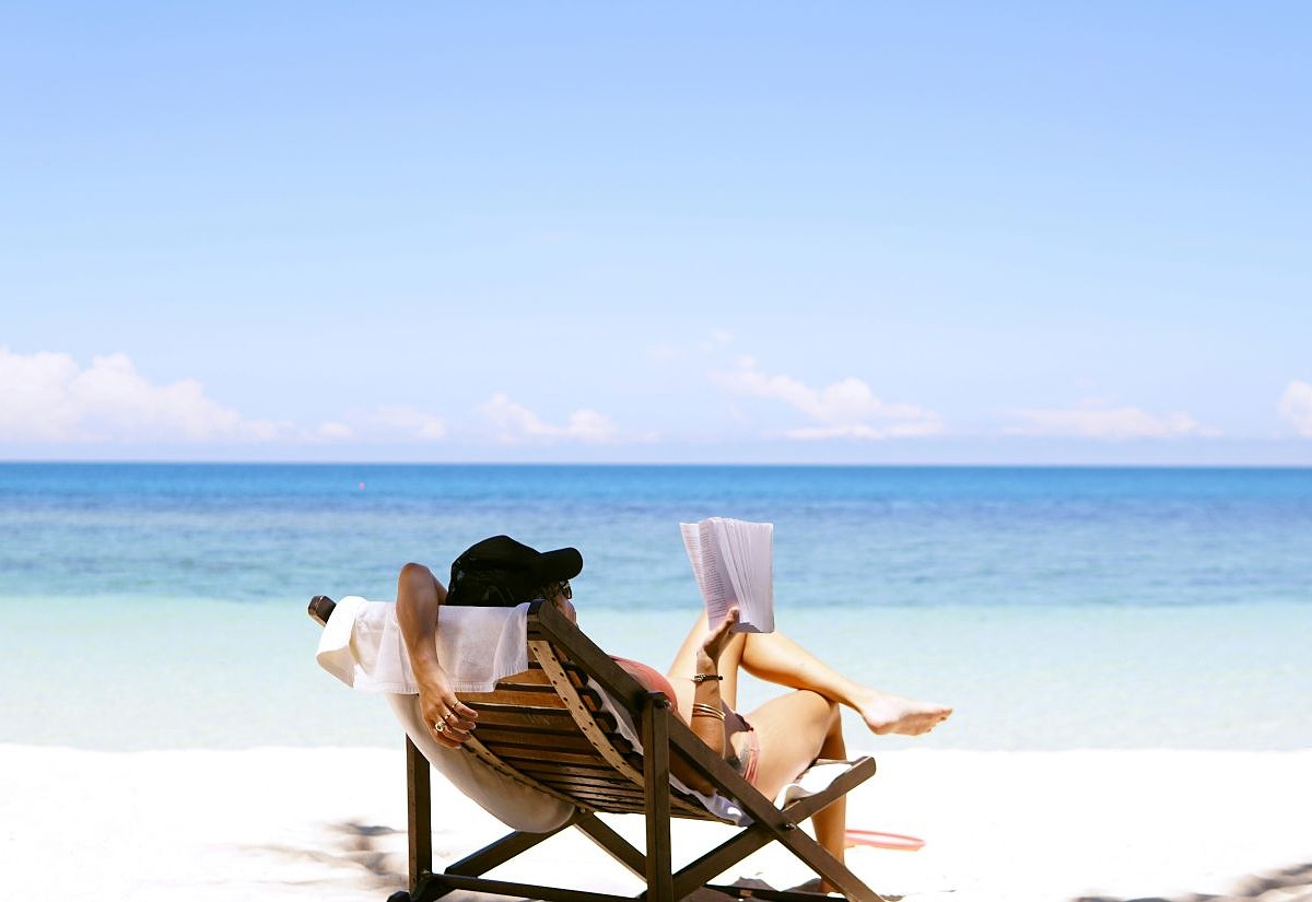 Urlaubsstimmung. Frau auf Liegestuhl am Strand, lesend