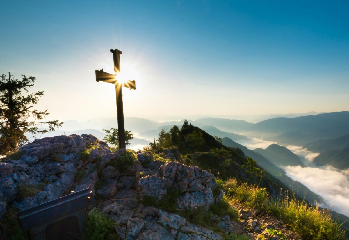 Kreuz auf Berggipfel im Gegenlicht
