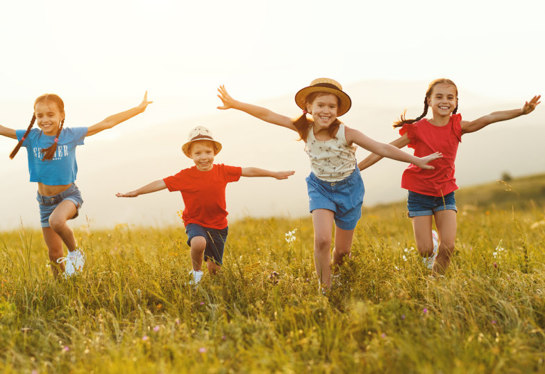 Fröhliche kleine Kinder in lässiger Kleidung haben Spaß, rennen gemeinsam über ein grünes Feld bei Sonnenuntergang