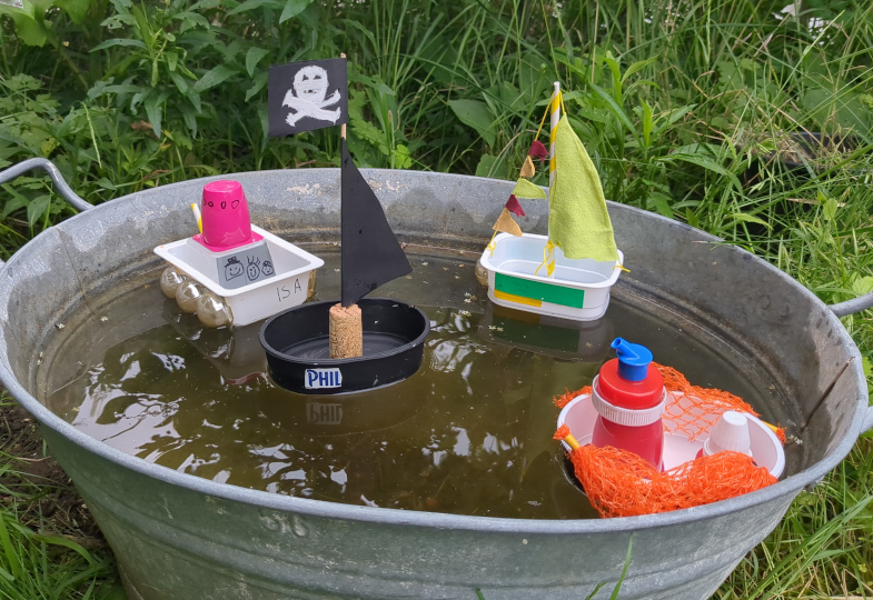 Boote aus Recyclingmaterialien in einem Eimer mit Wasser