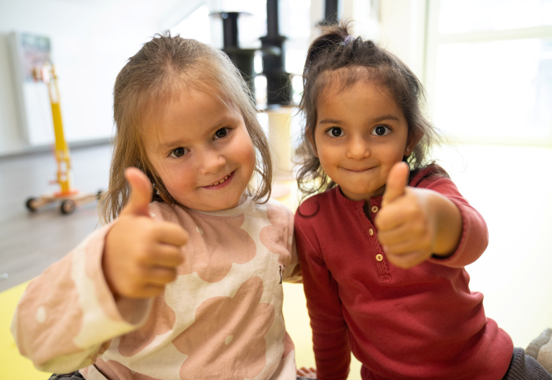 Zwei Kinder zeigen einen Daumen nach oben in die Kamera.