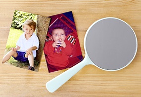 Zwei Kinderfotos liegen neben einem Handspiegel auf einem hölzernen Untergrund.