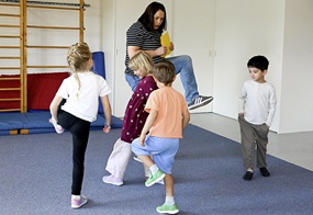 Vier Kinder und eine Fachkraft wandern mit erhobenen Füßen durch die Turnhalle.
