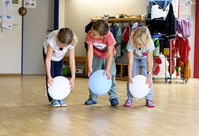 Mit Luftballons in der Hand bewegen sich drei Kinder zu entspannter Musik.