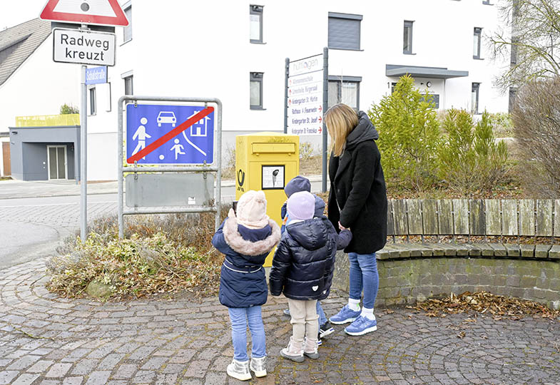 Kinder stehen mit einer erwachsenen Person vor Verkehrsschilder