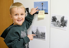 Ein Kind zeigt auf eine Wand mit Bildern und Notizzetteln von früheren Berufen wie Laternenanzünder und Kutscher.