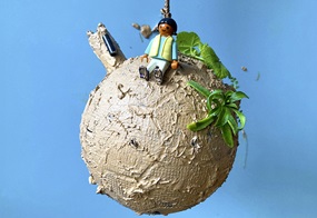 Eine Matschkugel hängt an einer Schnur, darauf sitzt ein Playmobilfigürchen umgeben von grünen Plastikpflanzen.
