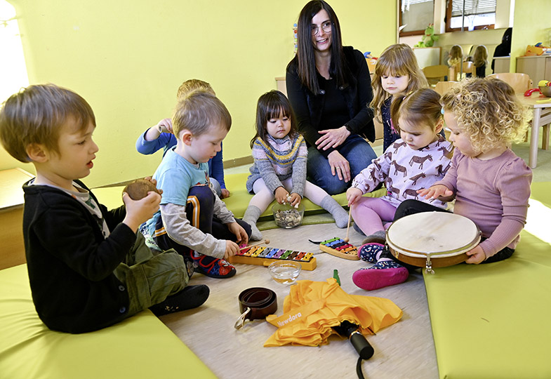 Kinder sitzen mit einer erwachsenen Person im Kreis