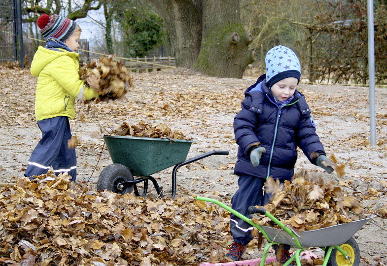 Kinder laden Laub in Schubkarren