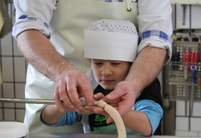 An der Füllmaschine machen die Kinder mit Unterstützung der Metzgers eigene Wurst