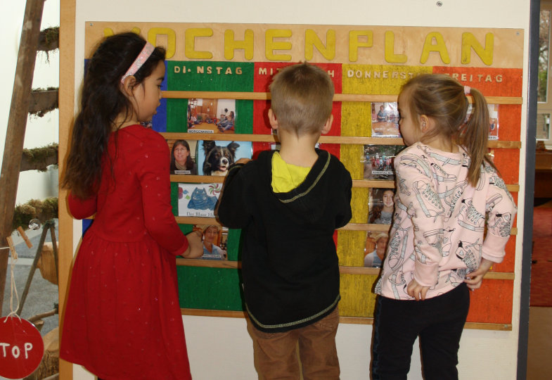 Drei Kinder schauen sich den Wochenplan in der Kita an