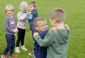 Die Kinder stehen auf einer Wiese, halten sich an den Schultern und schauen sich an.