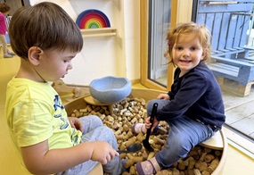 Die Kinder sitzen an einer Wanne mit Korken und halten Kellen zum Schöpfen in den Händen.
