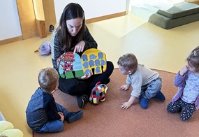 Kinder sitzen mit einer erwachsenen Person auf dem Boden