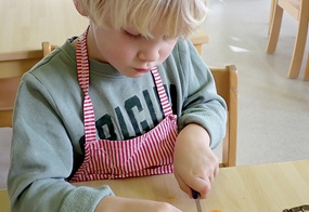 Ein Kind schneidet konzentriert Karotten in Würfelchen.