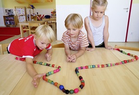 Kinder fädeln Perlen auf.