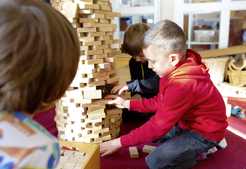 Kinder spielen mit einem Holzturm aus Klötzen