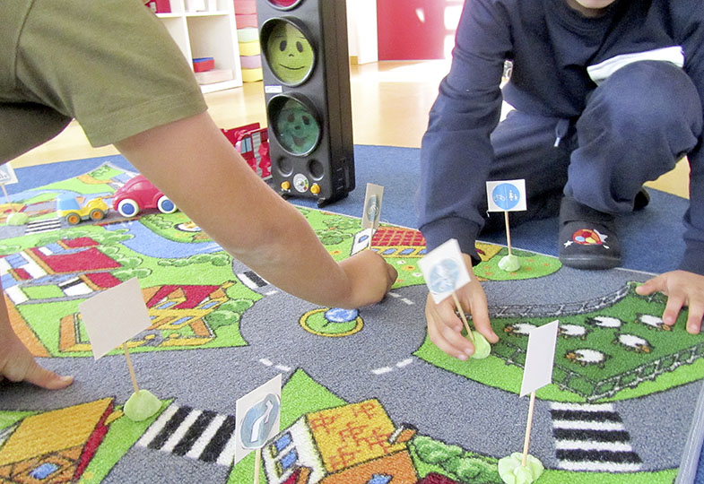Kinder spielen auf einem Teppich, auf dem eine Straße abgebildet ist