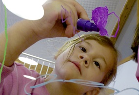 Ein Kind malt mit einem lila Stift auf einer Glasscheibe.