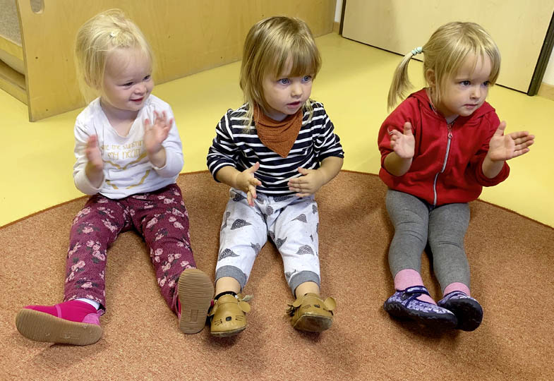 Drei Kinder sitzen auf dem Boden und klatschen in die Hände