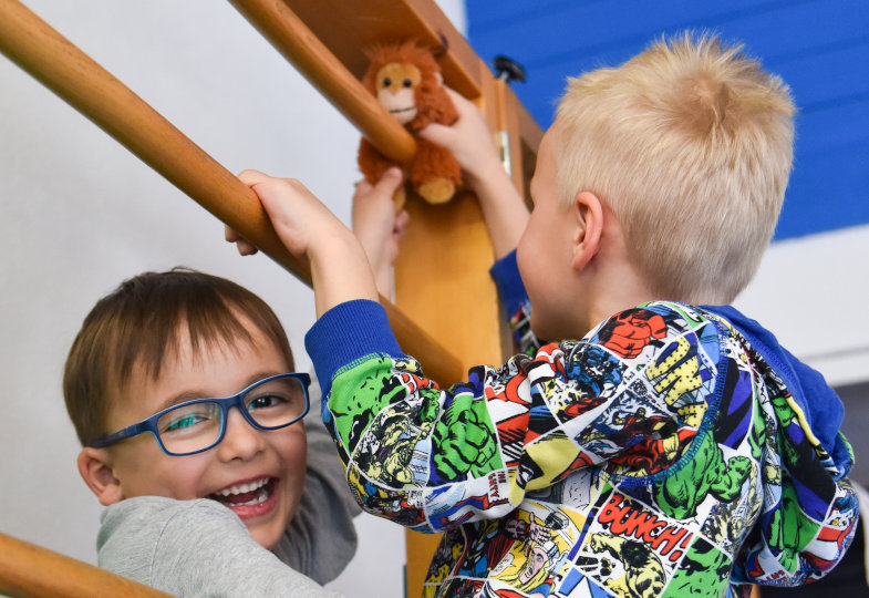 Zwei Kinder mit einem Plüschaffen an der Kletterwand