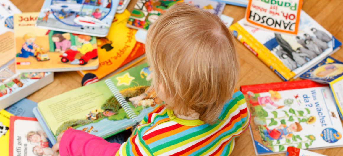 Kind sitzt mit vielen Büchern am Boden