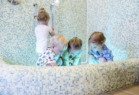 In einem Becken mit blauen Mosaikfliesen sitzen die Kinder und experimentieren mit Wasser.