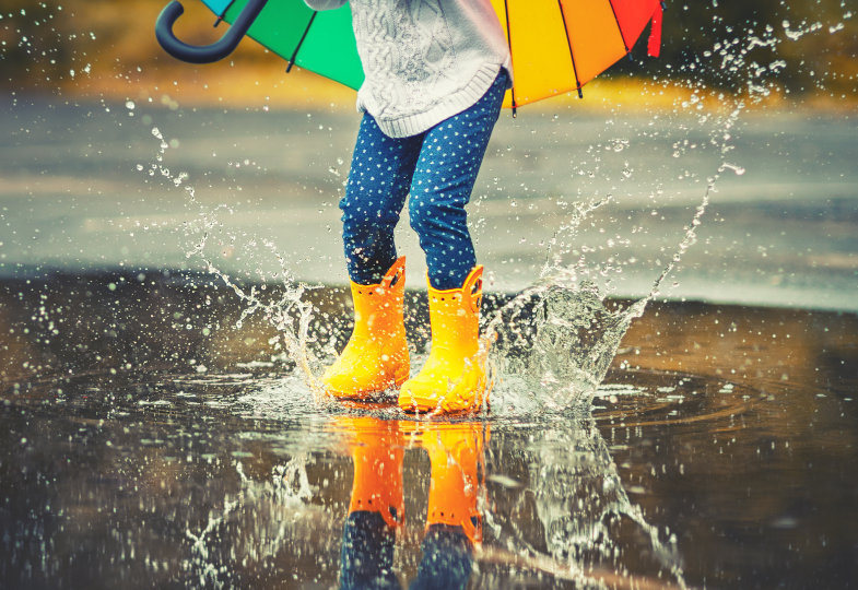 Kind springt mit Gummistiefel in eine große Pfütze