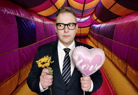 Ein Mann hält einen Herzluftballon und in der anderen Hand eine verwelkte Sonnenblume.