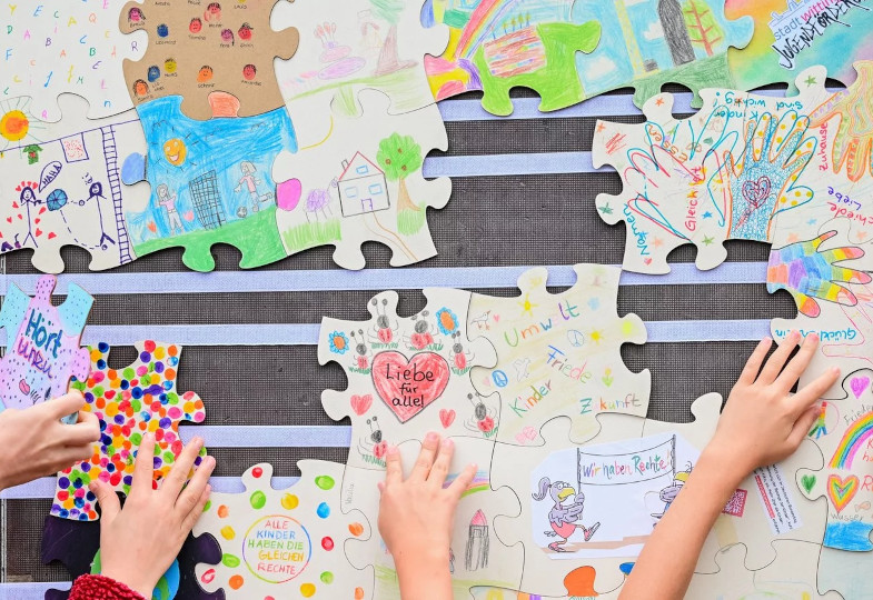 Bemalte Puzzlestücke und Kinderhände.