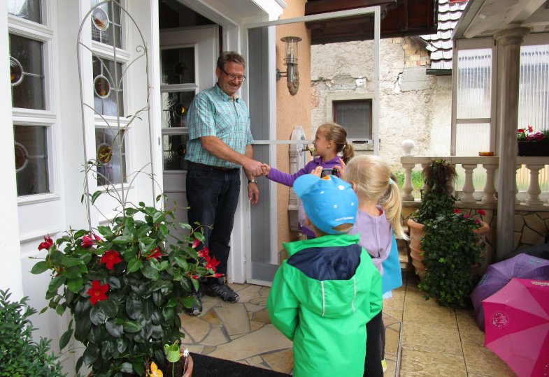 Kinder vor einer Haustür, aus der eine erwachsene Person kommt