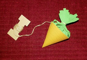 Eine aus Papier gebastelte Rübe hängt an einer aufgewickelten Schnur auf einem roten Stoffhintergrund.