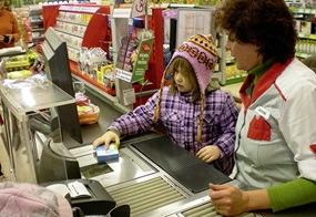 Ein Kind sitzt gemeinsam mit einer Verkäuferin an der Kasse und zieht konzentriert Produkte über den Scanner.