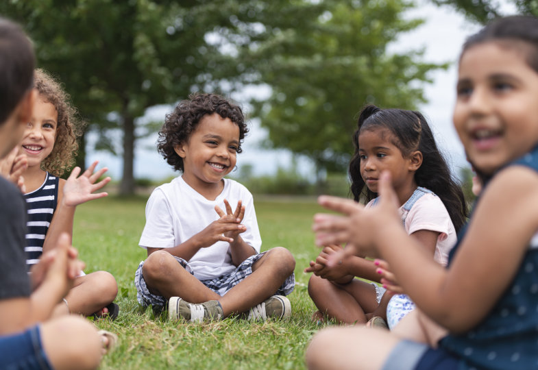 Kinder sitzen im Kreis im Garten und klatschen in die Hände