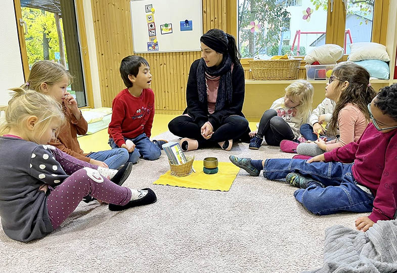 Kinder sitzen mit einer erwachsenen Person auf dem Boden im Kreis