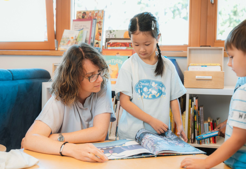 Drei Kinder blicken in ein Buch.