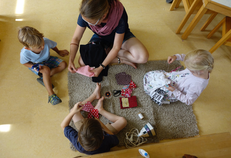 Kinder sitzen mit Nähmaterialien auf dem Boden