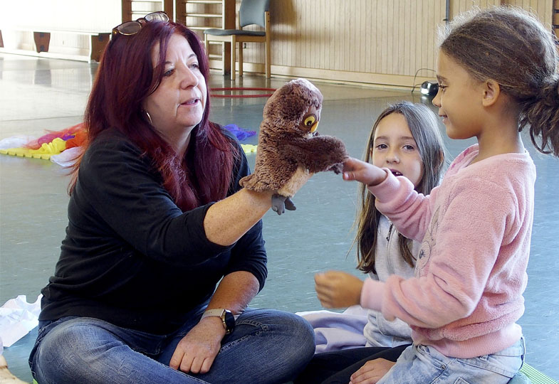 Erwachsene Person mit einer Handpuppe und zwei Kinder