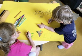 Zwei Kinder gestalten mit bunten Stiften ein Willkommensplakat für das Kita-Café.