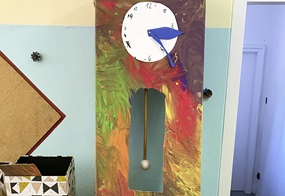 Eine selbstgebastelte Standuhr aus Karton in bunten Farben. 