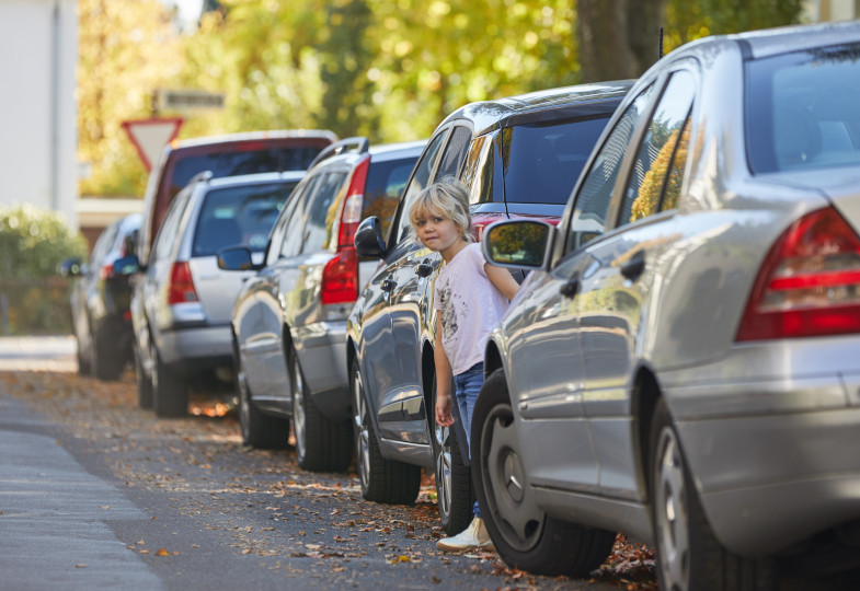 Ein Kind schaut auf einer Straße zwischen parkenden Autos hervor.