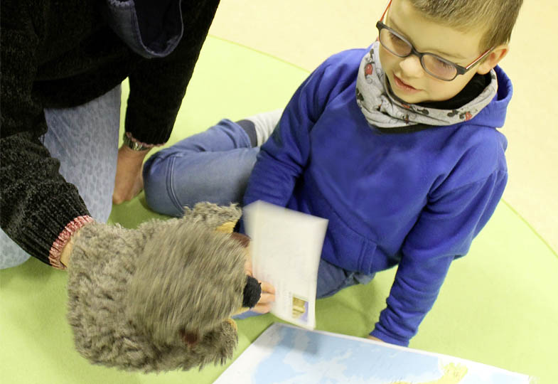 Kind schaut einer Handpuppe zu, die einen Briefumschlag in der Hand hält