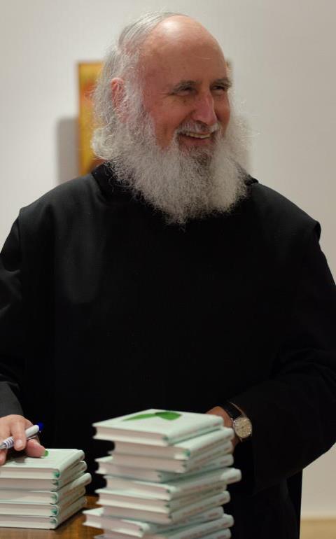 Porträt von Anselm Grün, wie er Bücher signiert.