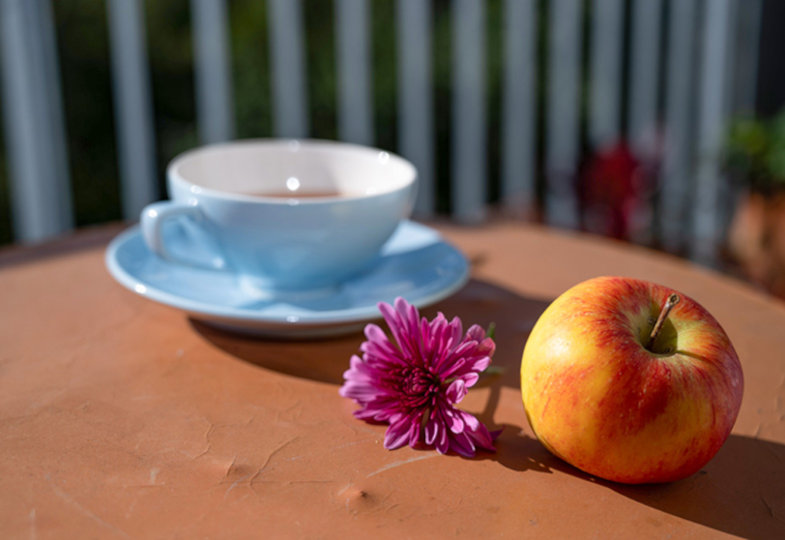 Ein Tisch mit einer Teetasse, einer lila Blume und einem Apfel 