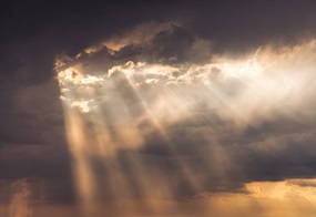 Durch große dunkle Wolken brechen einige Sonnenstrahlen hindurch.