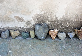 Steine in Herzform stehen an einer Mauer.