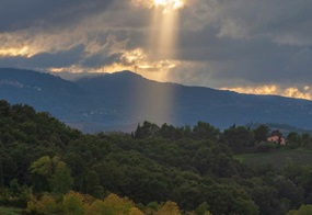 Sonnenstrahlen brechen durch eine Wolkendecke und scheinen auf bewaldete Hügel